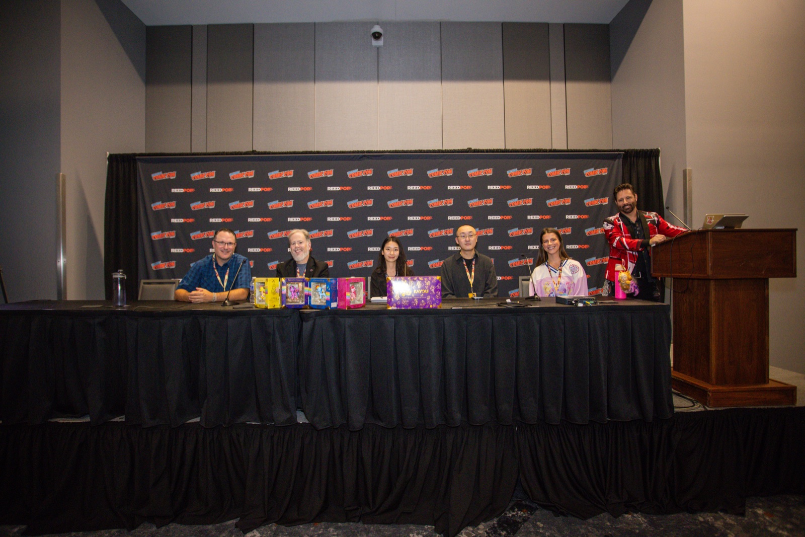 Six panelists seated at a long table in front of a New York Comic Con backdrop