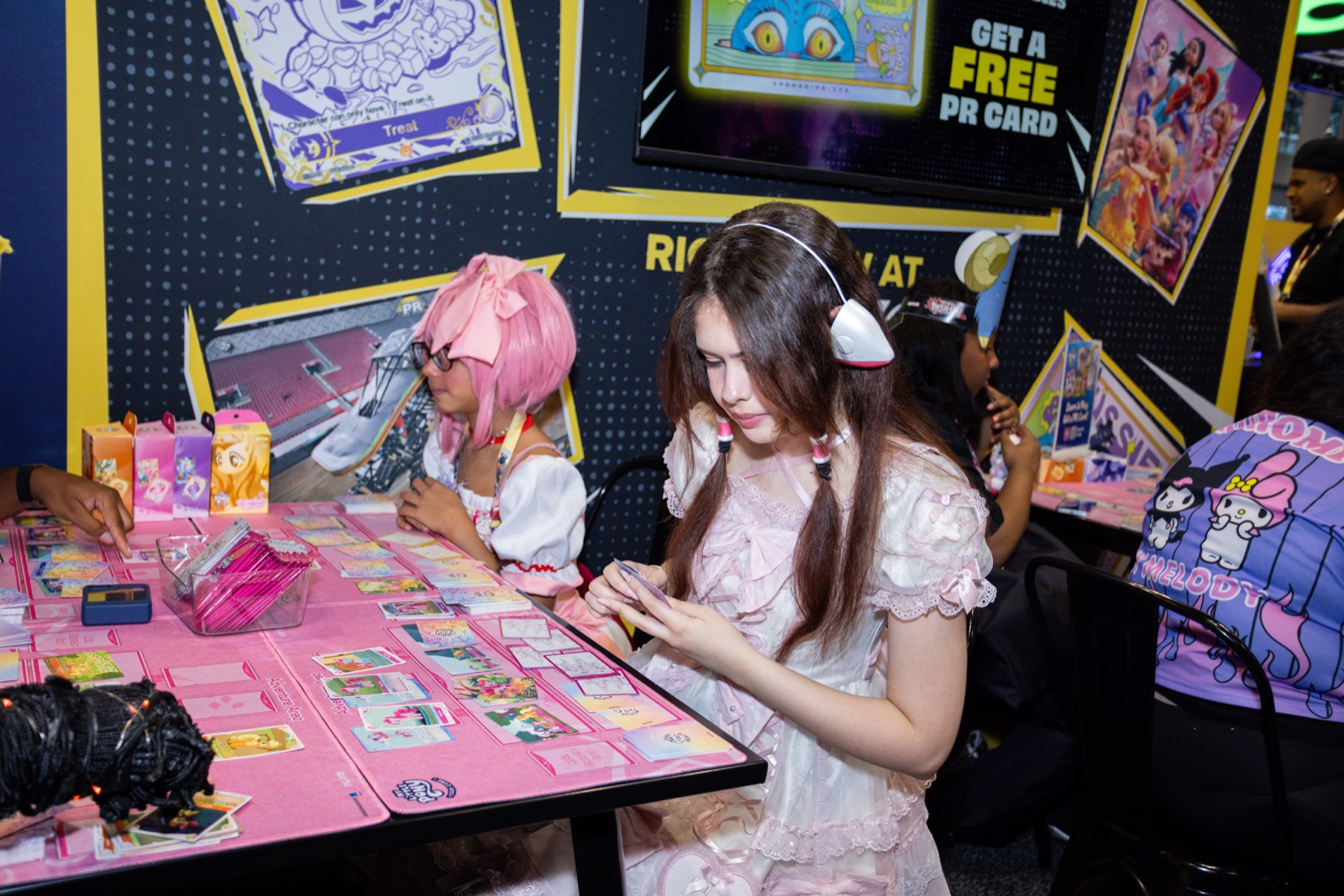 Fans playing the My Little Pony Trading Card Game on pink play mats at the KAYOU booth