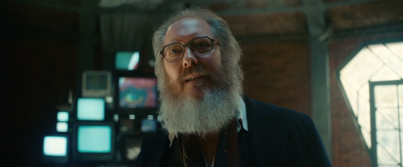 Ultron in his human avatar, a bearded man in glasses, in an attic full of glowing monitors